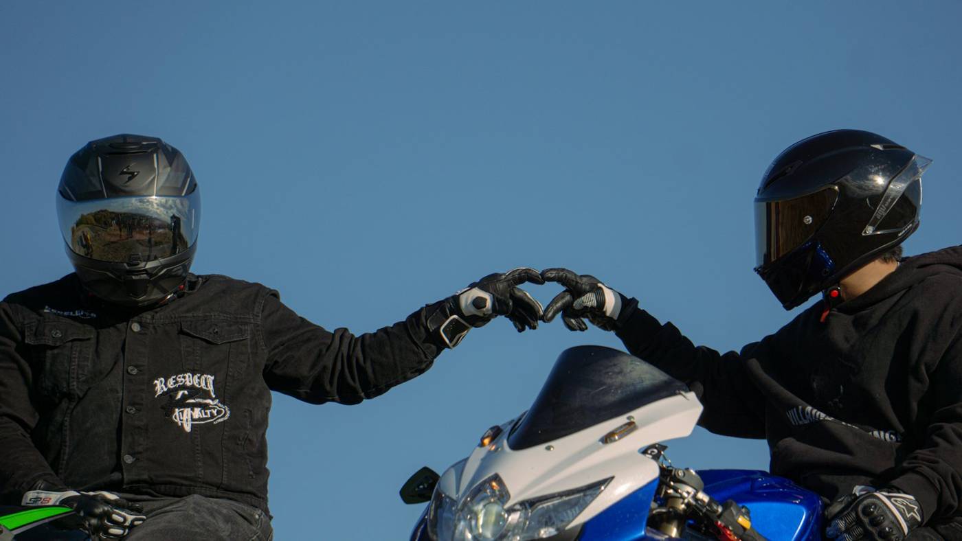 Two motorcycle riders in helmets making a heart shape with their gloved hands