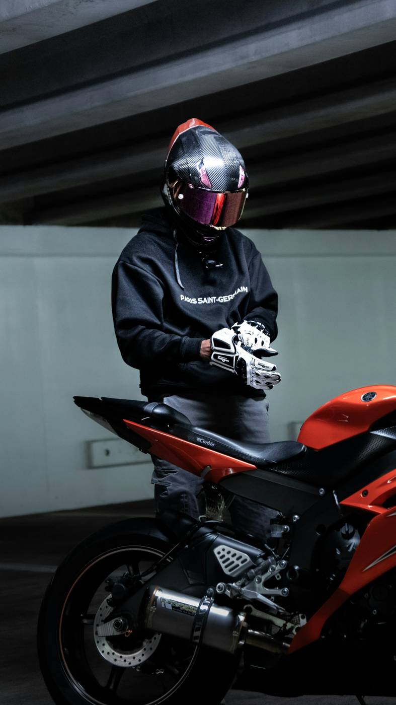Motorcyclist in a helmet pulling on riding gloves beside a sport bike