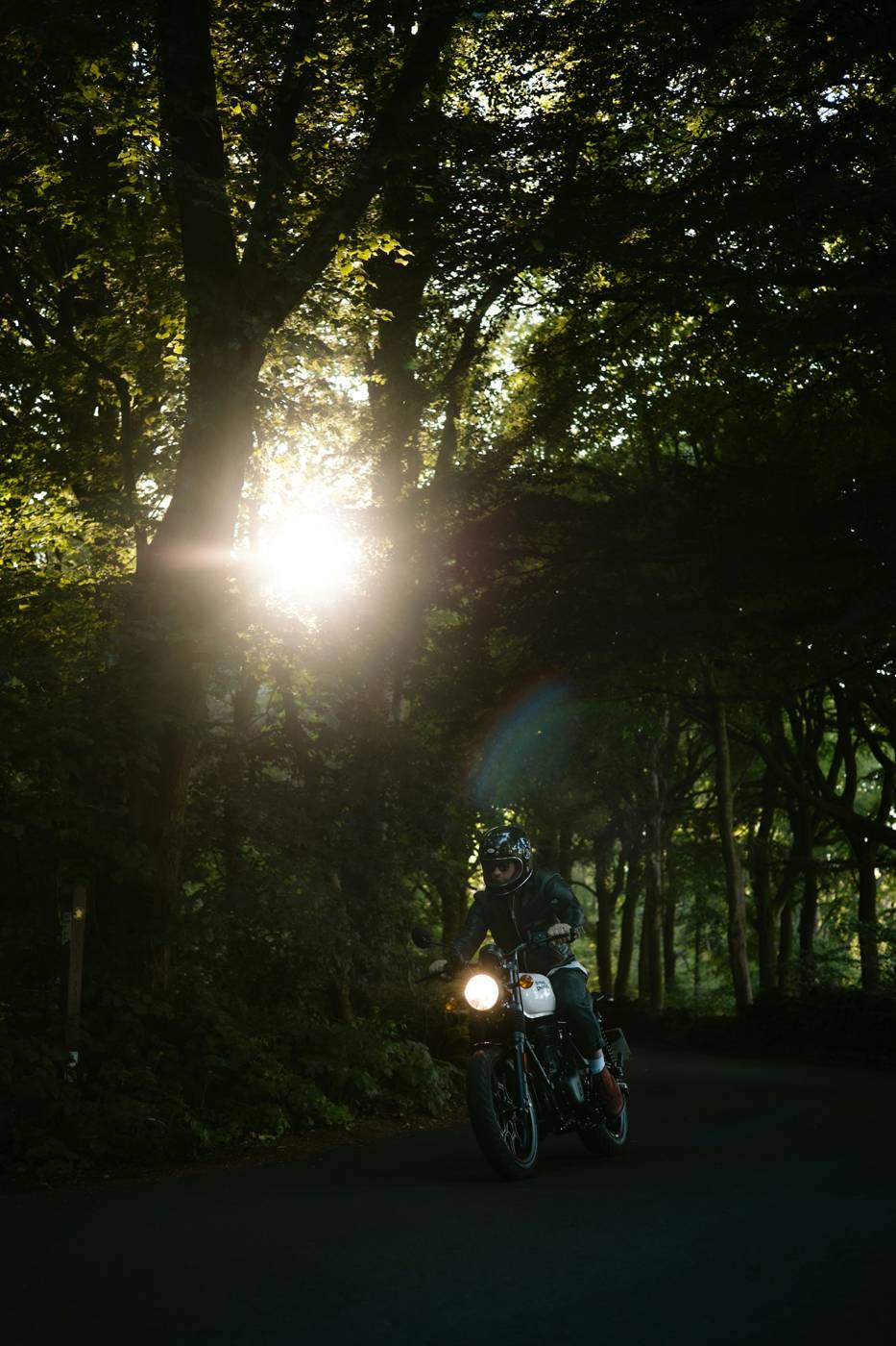 Morning ride Motorcyclist riding through a sunlit forest road