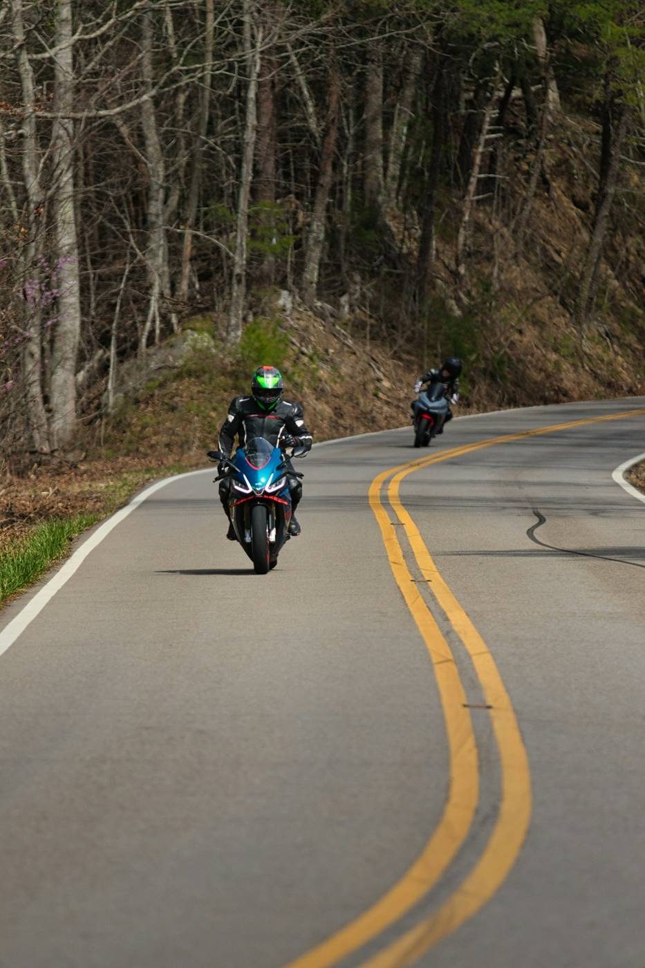 Two riders, one road Two motorcyclists riding a winding wooded road